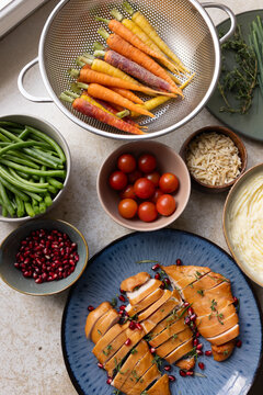Sliced chicken breasts are resting on blue plate on counter, with thyme and pomegranate arils