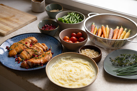 Glazed chicken resting on blue plate near window, bowls holding mashed potatoes and carrots