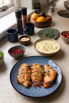 Blue ceramic plate holding three sliced salmon fillets, thyme and pomegranate arils near window