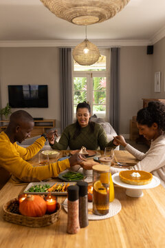 African American family holding hands in sweaters bowing heads at home table with pie and candles