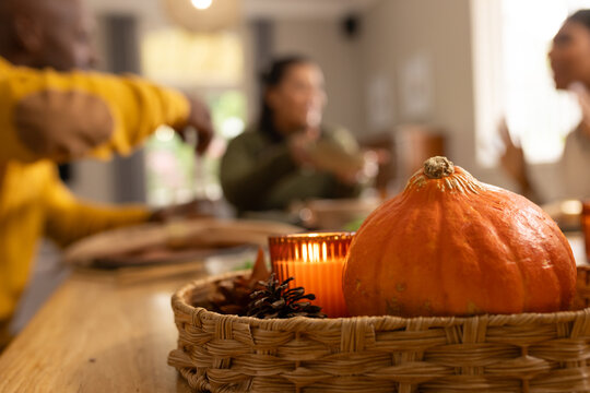 African American friends chatting at table with pumpkin in wicker basket and lit candle, copy space