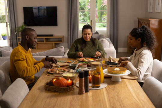 African American family sitting at dining table wearing knitwear and sharing pie near French doors