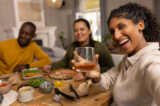 African American friends raising short glass, sitting at home table with plates, copy space