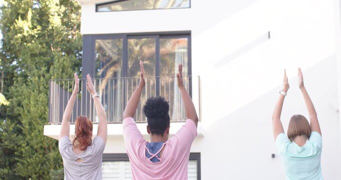 Diverse women after cue raising arms, palms touching, balancing in tree pose front yard in leggings