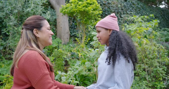 African American mother coming arms open, embracing daughter for portrait in garden coral sweater