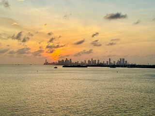 Fototapeta premium A scenic seascape capturing a vibrant orange and yellow sunset sky over calm sea waters with faint city silhouettes on the horizon