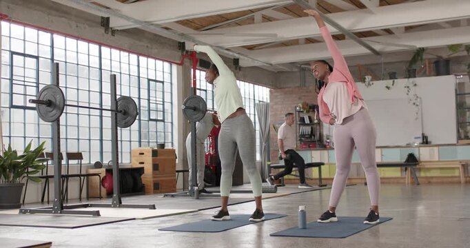 African American women starting warm-up, raising arm and bending sideways at gym on blue mats