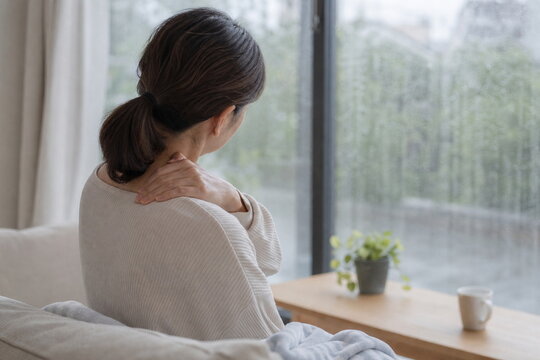 雨の日に首肩を押さえる後ろ姿の女性