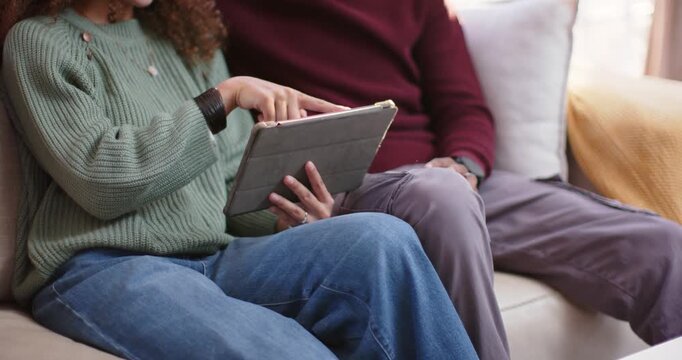 Couple sitting on couch, woman tapping tablet folio while man leaning in viewing pictures