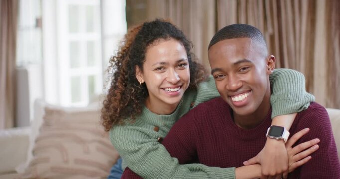 Diverse couple on sofa, woman coming behind, hugging partner, laughing, showing affection, ring