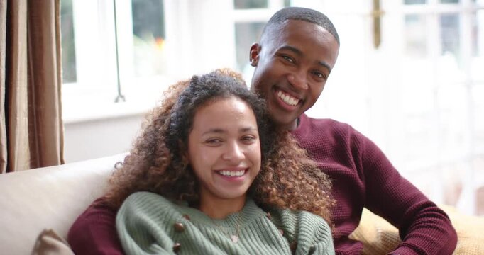 Diverse couple cuddling in sweaters after woman leaning into man's arm, showing affection on sofa
