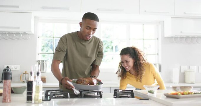Diverse couple watching man bringing hot roast pan onto gas stove using towel, checking roast