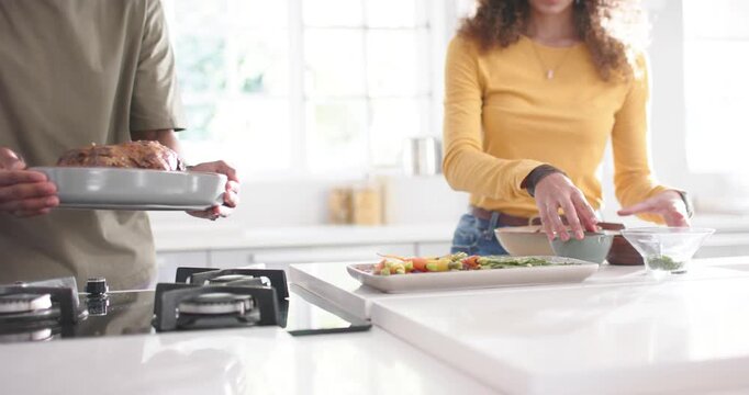 Diverse couple plating at island counter as man bringing roast, woman mustard-top aligning bowls