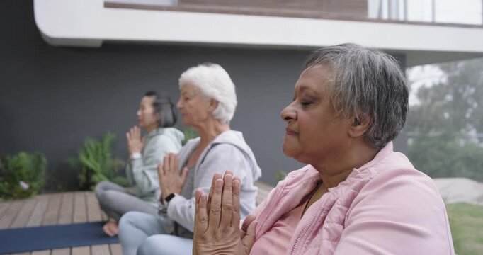 Senior women friends sitting on yoga mats on deck, finishing meditation, opening eyes, smiling