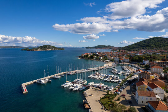 Drone shot capturing the coastal town of Preko on Ugljan island, Croatia. Scenic view of the Adriatic sea, local harbor with moored yachts, traditional red-roof houses, and neighboring islands.
