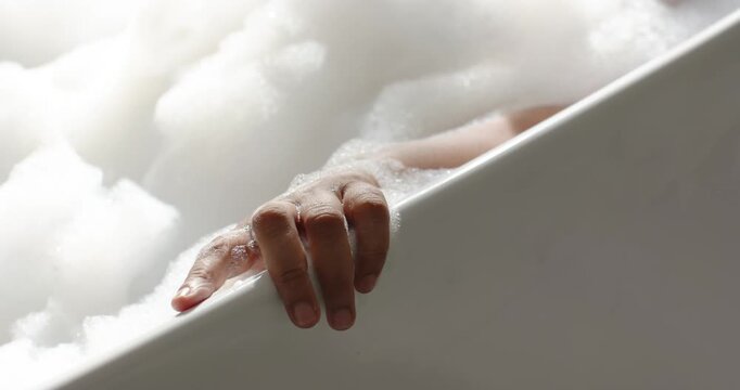 African American woman resting hand on tub rim, soapy fingers sliding then settling while bathing