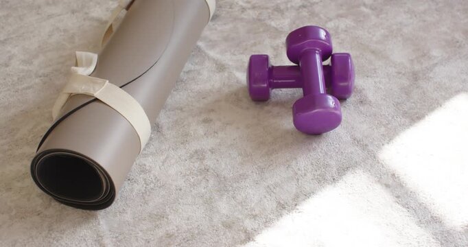 Camera is tightening frame, bringing rolled mat and purple weights closer to sun patch near window