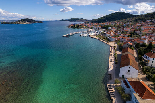 Drone shot capturing the coastal town of Preko on Ugljan island, Croatia. Scenic view of the Adriatic sea, local harbor with moored yachts, traditional red-roof houses, and neighboring islands.
