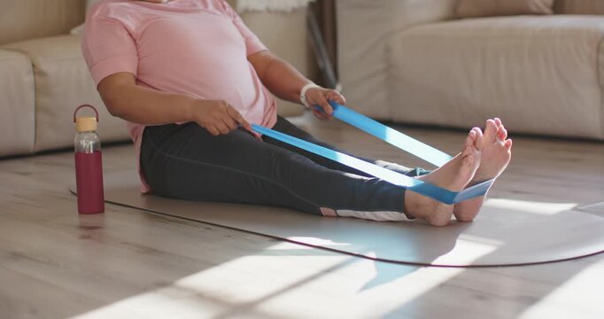 Mature woman starting looping blue resistance band around feet, pulling for strength on home mat