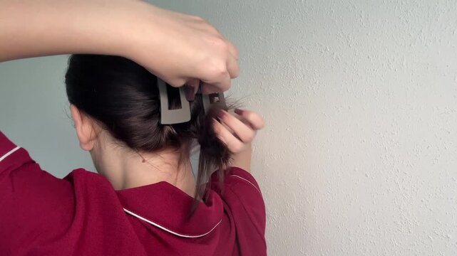 Woman gathering long dark hair, twisting strands into a quick updo, securing an everyday hairstyle with a fashionable plastic claw clip, demonstrating a simple daily beauty routine.