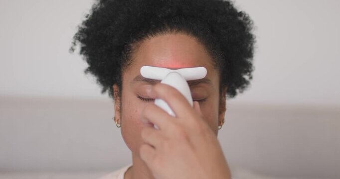 African American adult using white T device pressing brow sliding nose for LED skincare in bedroom