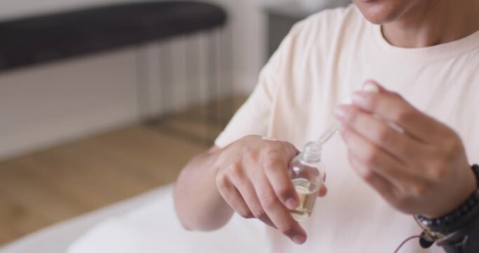 African American man opening dropper drawing oil applying to hand smelling to test at spa table