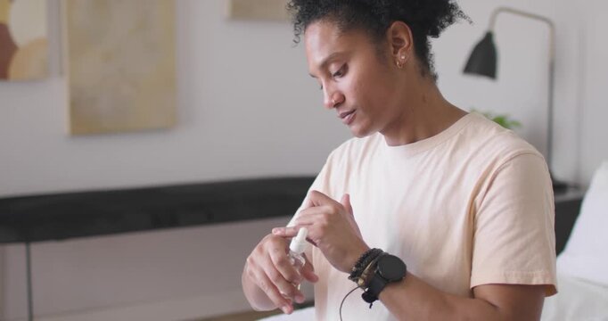 African American man priming and pressing small white pump bottle in bedroom, dabbing skincare