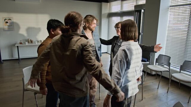 Caucasian female psychotherapist leading diverse support group in standing up, hugging, and clapping during therapy session. Video for mental health awareness and wellness campaigns