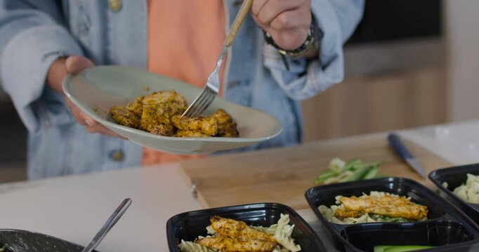 African male in denim jacket stabbing chicken, forking into three meal boxes at counter for lunches