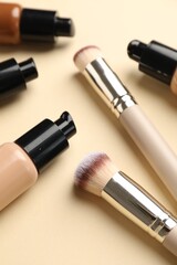 Obraz premium Makeup brushes and bottles of foundation on beige background, closeup