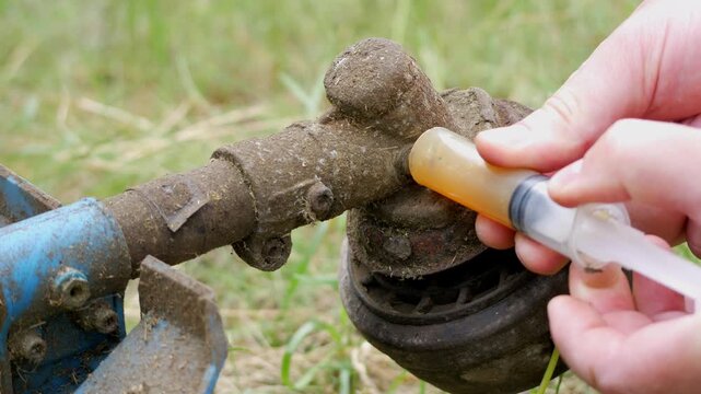 Man Lubricating Gearbox of Gas Powered String Trimmer During Maintenance