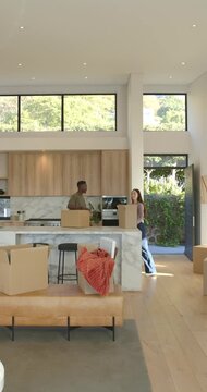 Vertical video: Diverse couple unpacking behind marble island, woman arriving with box, settling in