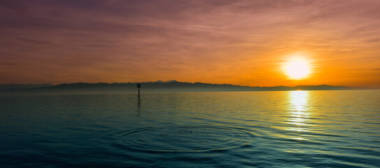 Fototapeta premium Malerischer Sonnenuntergang in Wasserburg am Bodensee mit Blick auf das Alpenpanorama und Wasserringen im Vordergrund