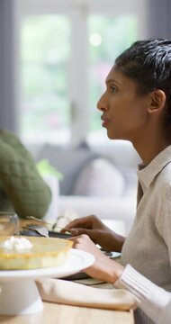 Vertical video: Two friends sitting at table while talking, woman cutting pie with fork, copy space