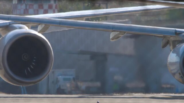 Jet engine and airplane wing taxiing on airport tarmac with heat haze distortion under bright sunlight, telephoto close-up shot
