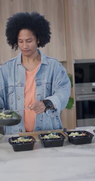 Vertical video: African American man at kitchen counter scooping from pan, filling black meal trays