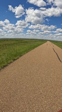 POV while driving on a narrow farmland road under a spectacular blue summer sky with white cumulus clouds and the sun in the upper left corner
