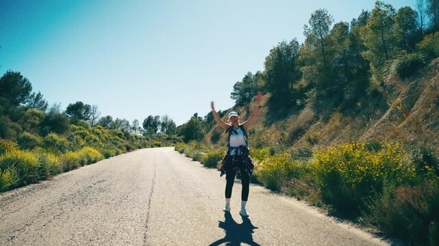 Young female traveler with a backpack hitchhiking on a scenic country road surrounded by nature. Freedom, adventure, courage, independence and pursuing dreams concept during a solo journey.