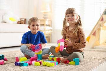Naklejka premium Little kids playing with colorful blocks on floor at home