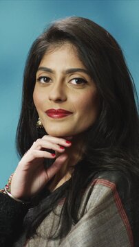 Close up portrait of beautiful Indian woman holding chin with hand and looking at camera with grace. Female wearing traditional clothing in light room. Elegant pose showing confidence and calm mood.
