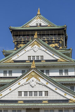 View of the ornate upper tiers of Osaka Castle featuring green tiled roofs and gold leaf decorations under a clear blue sky in Osaka, Osaka, Japan.