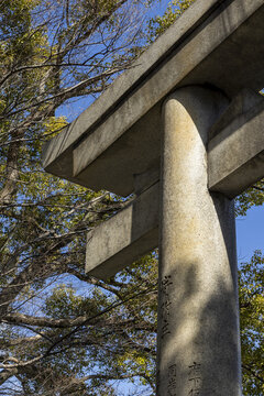 View of a traditional stone torii gate with weathered textures against a backdrop of green trees and a clear blue sky in Osaka, Osaka, Japan.