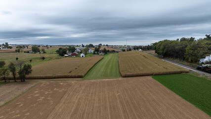 Fototapeta premium Cornfields line the land with a few houses visible in the distance. A railway track runs along the edge of the fields as clouds fill the sky. The scene shows rural life on a fall day.