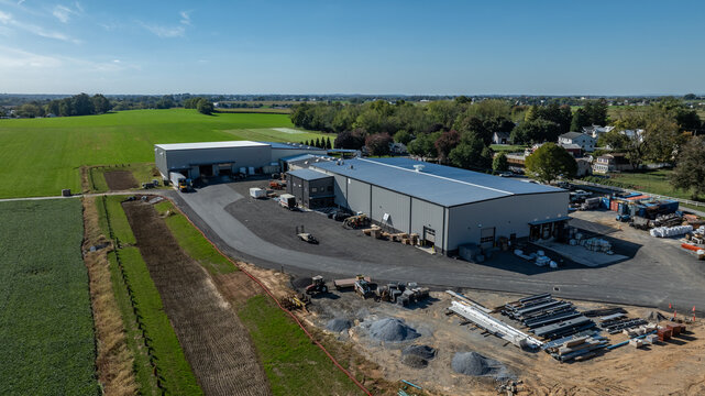 Construction takes place at a large site surrounded by green fields and few buildings. Workers and machinery are active during the day.