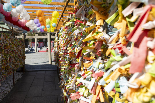 View of colorful paper prayer strips tied to a wooden frame and hanging lanterns at a traditional shrine in Osaka, Osaka, Japan.