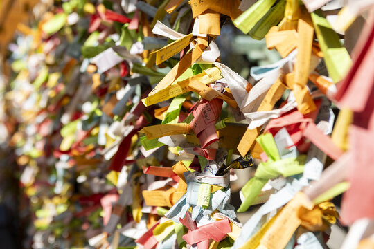 View of colorful omikuji fortune paper strips tied to a wooden rack at a Shinto shrine under bright sunlight Osaka, Osaka, Japan.