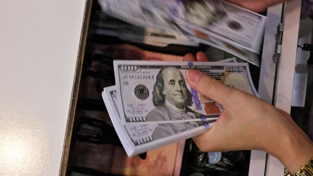 Closeup of a persons hand counting a stack of one hundred us dollar bills from a cash register drawer
