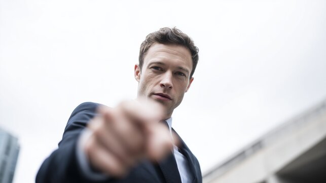 Businessman pointing finger directly at viewer with serious expression, low angle view