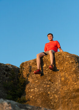 Young man sitting on mountain rock peak enjoying success