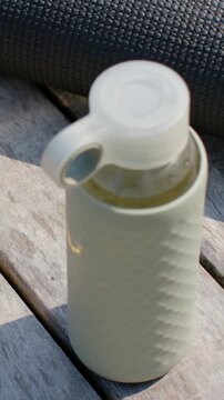Vertical video: Tilting camera revealing reusable bottle with clear cap loop and droplets on deck